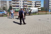 Fotografia kolorowa. Na zdjęciu widoczny policjant stojący tyłem pokazujący coś do zebranych na boisku dzieci.