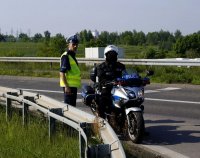 Fotografia kolorowa. Na zdjęciu policjant w kamizelce odblaskowej obok policjanta siedzącego na policyjnym motocyklu.