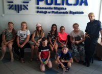 Zdjęcie na tle napisu Komenda Miejska Policji w Piekarach Śląskich. Na zdjęciu pozujące dzieci wraz z policjantką w mundurze.