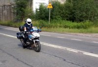 Fotografia kolorowa. Na zdjęciu widoczny policjant na motocyklu.