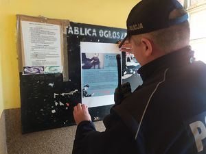 Zdjęcie przedstawia dzielnicowego, który wiesza na tablicy ogłoszeń plakat informacyjny
