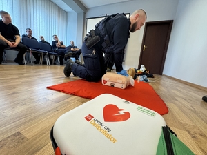 Zdjęcie przedstawia defibrylator oraz policjanta ćwiczącego pierwszą pomoc